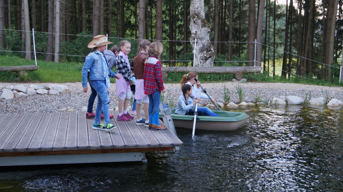 Kinder auf dem Steg am Teich, zwei im Boot
